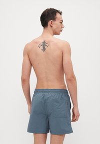 Costumi da bagno grigi da uomo con vita elastica e tasca laterale; texture liscia; senza fantasie; indossati da un modello visto di spalle.