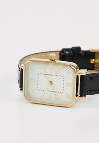 Reloj de pulsera rectangular de color dorado con una cara blanca, números romanos y una correa de cuero negro. Cuenta con una corona para ajustar la hora.