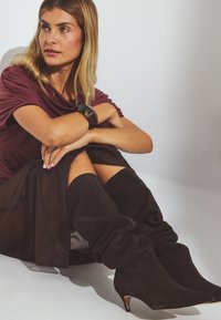 Čierne semišové čižmy po kolená s voľným dizajnom, špicatou špičkou a nižším podpätkom. Hladký povrch bez viditeľných vzorov alebo akcentov.