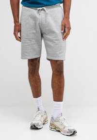Grijze katoenen shorts met een elastische tailleband en een trekkoord. Eenvoudig ontwerp, knielang, gecombineerd met beige en witte sportschoenen en sokken.