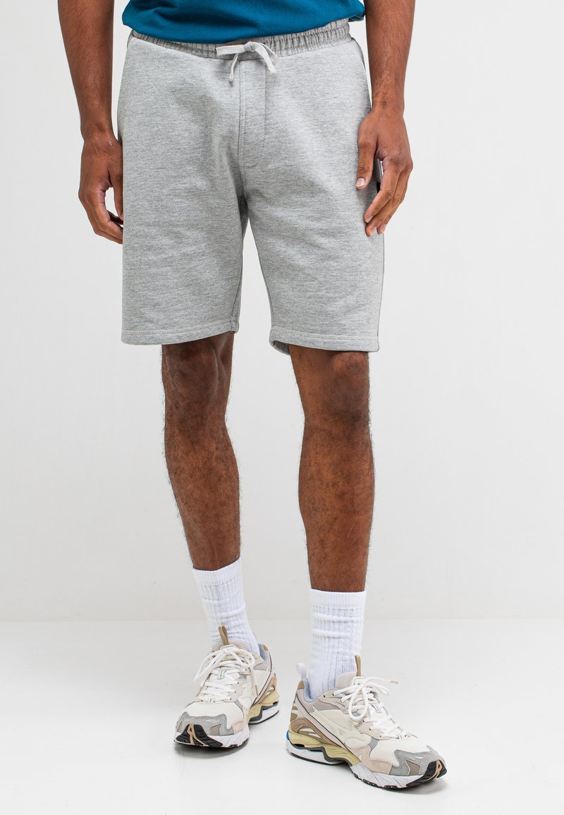 Grijze katoenen shorts met een elastische tailleband en een trekkoord. Eenvoudig ontwerp, knielang, gecombineerd met beige en witte sportschoenen en sokken.