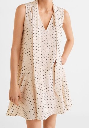 Robe sans manches beige avec des pois noirs, décolleté en V et détail drapé à l'avant. Jupe évasée et tissu léger.