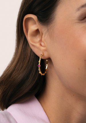 Pendiente de aro de oro con un diseño enlazado que incluye múltiples piedras preciosas, con acentos en rosa y púrpura, usado en la oreja.