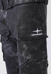 Schwarze Cargo-Hose mit strukturiertem Finish, ausgestattet mit einer Seitentasche und dem weißen PXP-Logo, das eine leicht ausgewaschene Optik zeigt.