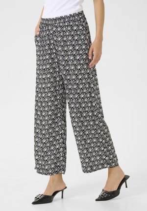 Black and white patterned wide-leg pants with an elastic waistband and side pockets, paired with black heeled mules.