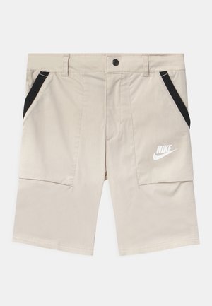 Shorts Nike beiges avec des accents noirs, dotés de deux poches latérales et d'une texture lisse. Logo imprimé en blanc sur la cuisse gauche.