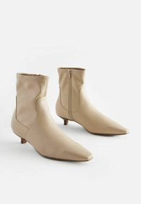Beige ankle boots made from smooth synthetic material. Features a pointed toe, low heel, and zipper closure at the back for easy wear.