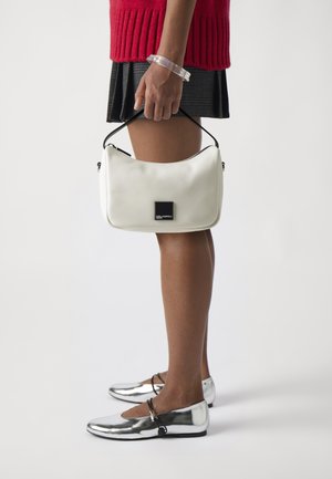White leather handbag with a curved shape and black logo patch, paired with a black flared skirt and shiny silver ballet flats.