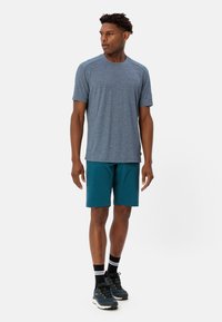 Outfit atletico composto da una maglietta azzurra a maniche corte e pantaloni corti turchesi. La maglietta ha una texture morbida; i pantaloni corti sono leggeri e dotati di tasche.