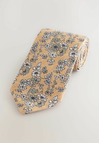 Cravate florale en tissu jaune avec des motifs de fleurs bleues et vertes intriqués. Le design enroulé met en valeur la texture et le détail de l'imprimé.