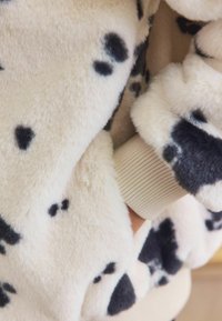 Fleece jacket with cream base and black spotted pattern. Features ribbed cuff peeking from the sleeve. Soft texture and relaxed fit.