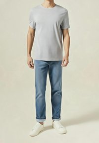 Graues Baumwoll-T-Shirt mit rundem Ausschnitt, kombiniert mit hellblauen Denim-Jeans, hochgekrempelten Säumen und weißen Sneakern. Einfaches, legeres Outfit.