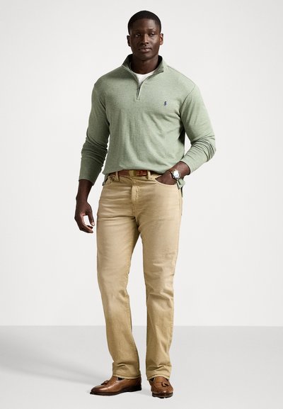Light green quarter-zip sweater, beige pants, and brown loafers with a watch. The sweater has long sleeves and a logo on the chest.