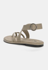 Beige platte sandaal met meerdere kruislussen, verstelbare enkelband met een ronde metalen gesp, zachte suède textuur en een zwarte rubberen zool.