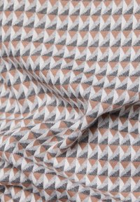 Nahaufnahme eines Stoffes mit einem sich wiederholenden Muster aus kleinen Dreiecken in Beige, Grau und Weiß, das die Textur und Falten zeigt.