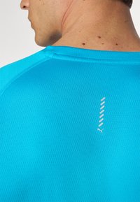 Lyseblå atletisk T-shirt med et struktureret mønster, der har et lille hvidt logo og designdetaljer på bagsømmens søm.