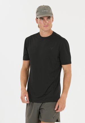 Ung mand iført en sort kortærmet skjorte, grå shorts og en grå kasket med "VIRTUS" logo på hvid baggrund.