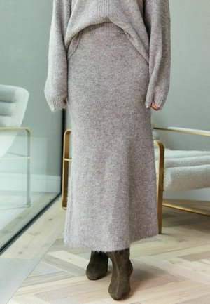 Lichtgrijze gebreide trui en bijpassende lange rok, gemaakt van zacht gestructureerde stof, gecombineerd met olijfgroene enkellaarzen. Minimalistisch ontwerp.