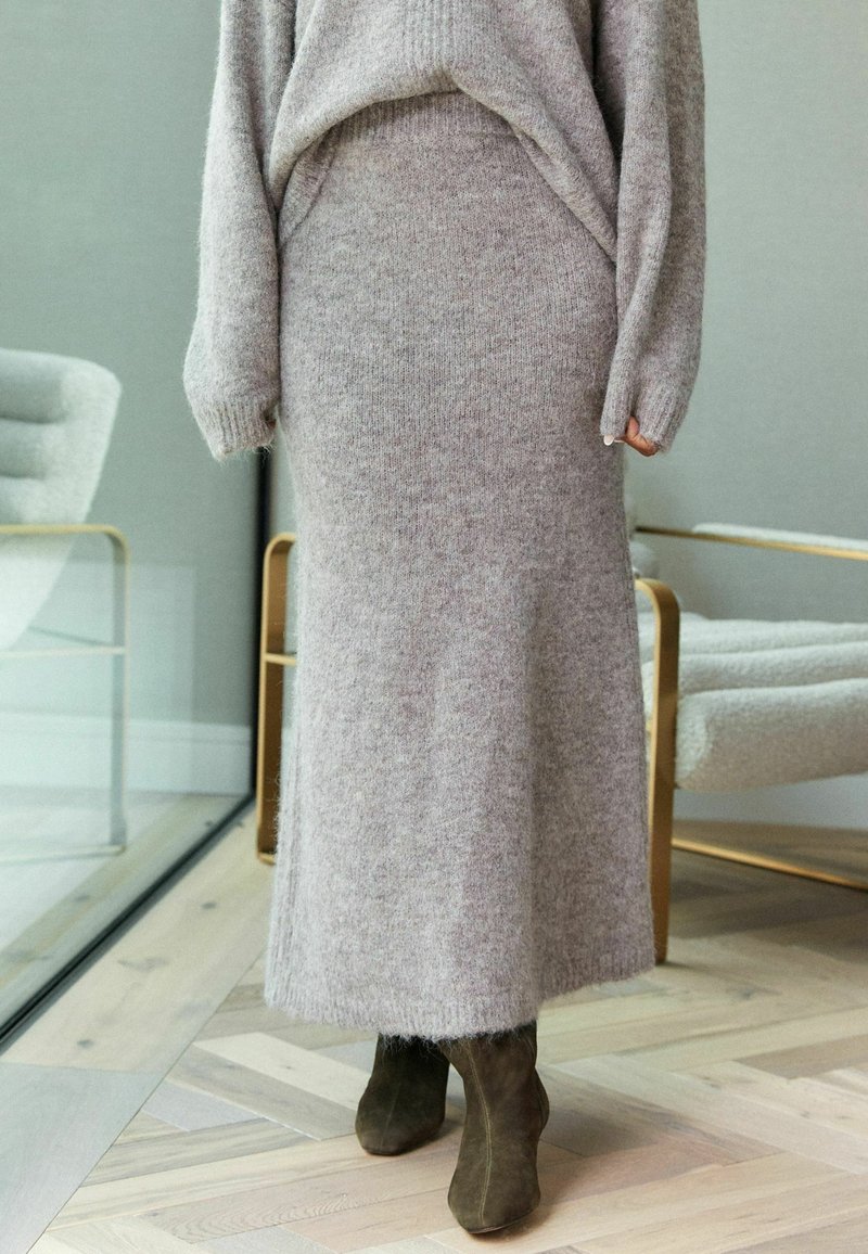 Pull tricot gris clair et jupe longue assortie, fabriqués en tissu doux à texture agréable, combinés avec des bottines vert olive. Design minimaliste.