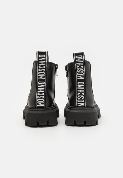 Botas de cuero negras hasta el tobillo con una suela gruesa, que cuentan con un cierre de cremallera y una etiqueta de logo negro y blanco prominente en la parte trasera.