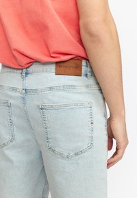 Lichtblauwe denim jeans met een soepele textuur, voorzien van een bruine leren achtertag, geperst met "REVOLUTION" en een klassieke vijfzakkenontwerp.