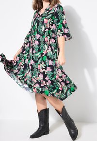 Robe noire à fleurs avec des motifs roses et verts, longueur genou avec des manches évasées ; associée à des bottes de cowboy noires. Tissu léger, design fluide.