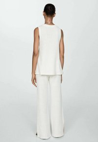 White knitted sleeveless top paired with wide-leg trousers, featuring a textured finish and side slits, from a back view.
