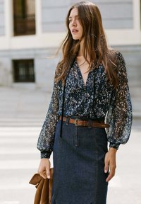 Blusa fluida e trasparente blu navy con stampa floreale e maniche ampie, abbinata a una gonnella in denim scuro e una cintura marrone con fibbia decorativa.