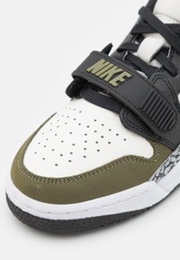 Šedé a bílé tenisky s olivově zelenými akcenty. Obsahují perforovanou špičku, texturovaný pásek a gumovou podrážku s vzorovaným detailem.