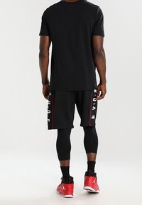 Svart sport t-shirt, svarta shorts med vit text, svarta leggings och röda basket skor. Fokusera på komfort och rörlighet.