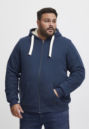Marine blauwe hoodie met rits, voorzien van een comfortabele lichtgekleurde fleece voering, voorzakken, witte trekkoorden en geribbelde manchetten aan de onderkant.