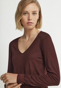 Bordeauxfarbener Pullover mit langen Ärmeln und V-Ausschnitt. Rippabschlüsse und eine glatte Textur betonen seine lässige Eleganz.