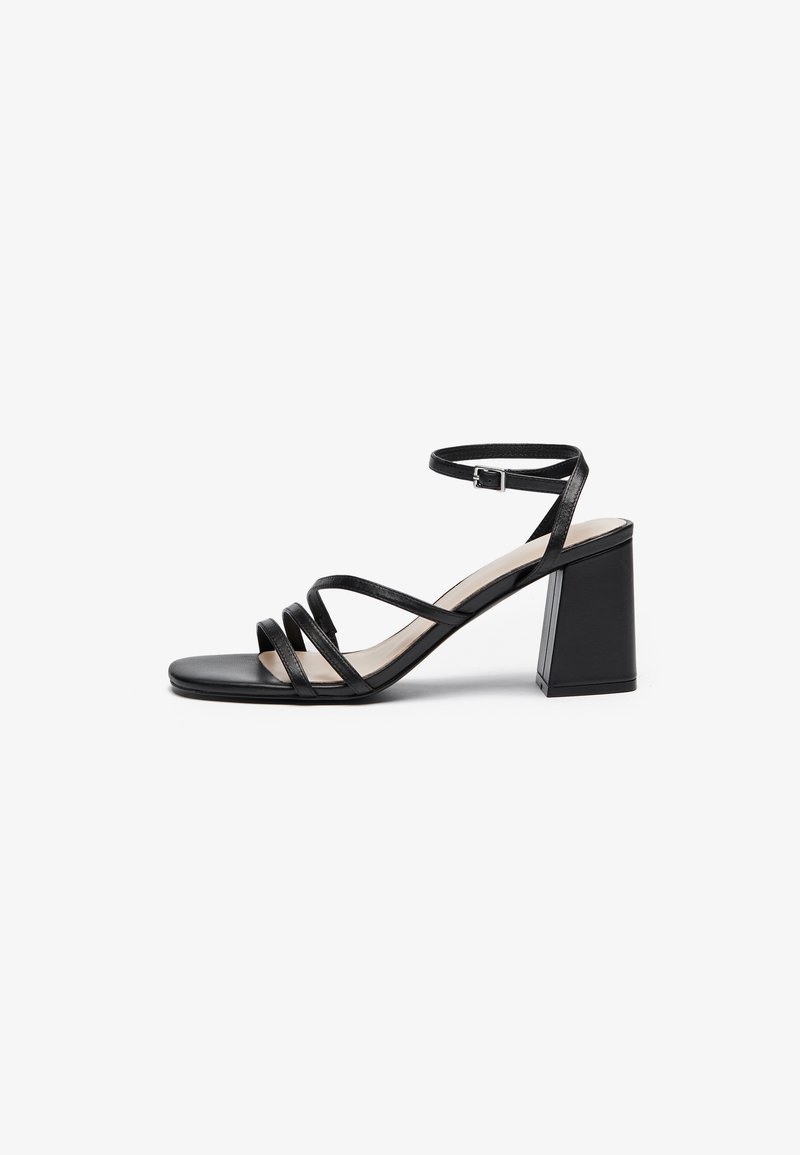 Black heeled sandals with multiple thin straps, square toe, and a block heel, featuring an adjustable ankle strap. Smooth leather texture.