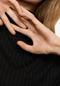 Due mani con le dita intrecciate poggiate vicino al collo e alla spalla di una persona, con lunghi capelli e una maglia nera a costine visibili.