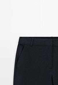 Navy tailored trousers with a flat waistband, side pockets, smooth fabric, and a crease down the front for a structured appearance.