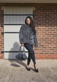 Veste grise, duveteuse, à double boutonnage avec de gros boutons, accents noirs, associée à des leggings noirs et un sac à main texturé de couleur sombre.