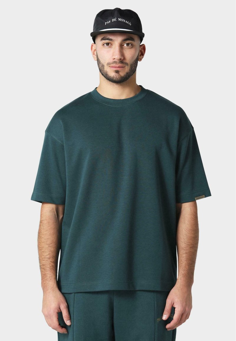 Tmavě zelené oversized tričko s krátkými rukávy a žebrovaným kulatým výstřihem. Hladká textura a minimální značení na lemu.
