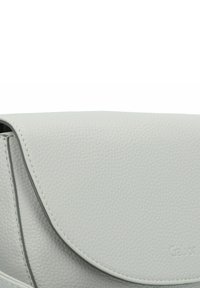 Borsa a tracolla in pelle grigia con chiusura a pattina arrotondata. Presenta un logo inciso discreto. Design pulito e minimale senza ulteriori decorazioni.