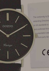 Montre analogique noire avec accents dorés, boîtier rond et design minimaliste. Comprend un cadran texturé et un bracelet en cuir. Certificat à proximité.