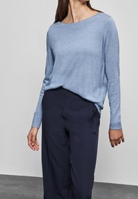 Vaaleansininen neulepaita, jossa on leveä pääntie ja pitkät hihat, yhdistettynä tummansinisiin housuihin. Pehmeä rakenne ja rento istuvuus.