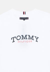 Λευκό βαμβακερό μπλουζάκι με καμπυλωτό λογότυ πο "TOMMY HILFIGER" σε σκούρο γκρι και κόκκινο. Ετικέτα με κόκκινες, λευκές και μπλε ρίγες στο λαιμό.