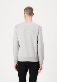 Sudadera gris de manga larga, con puños y dobladillo acanalados, textura suave, diseño sencillo, llevada sobre pantalones negros. Detalle de logo visible en los pantalones.