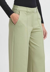 Svetlo zelene široke hlače z gladko teksturo, z stranskimi žepi in prilagojenim pasom z diskretnimi naborki.