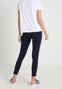 Marina leggings i stretchmaterial, åtsittande design, ankellång, kombinerad med en vit kortärmad topp och mönstrade skor utan snörning.