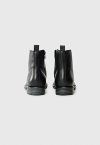 Bottines noires en cuir avec un talon bas, dotées d'une fermeture éclair à l'arrière et d'une languette de tirage, texture lisse et design simple et élégant.