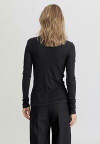 Zwarte lange mouwtop van ribmateriaal, met een aansluitende pasvorm, naaddetail langs de achterkant en zonder zichtbare accenten of patronen.
