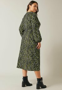 Vestido de manga larga negro y verde lima con estampado, con cintura ajustada, de corte midi y combinado con botines negros.