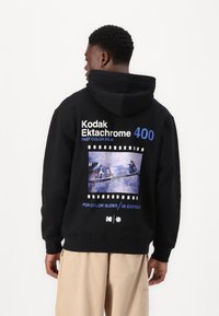 Black hooded sweatshirt featuring a Kodak Ektachrome 400 graphic, film strip design, and skateboard image. Soft texture and ribbed cuffs.