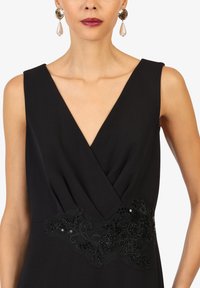 Robe noire sans manches avec un décolleté en V profond et une broderie complexe de perles noires autour de la taille ; présente une texture lisse et mate.
