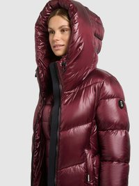 Bordeauxrode donsjas met hoge, verstelbare capuchon, glanzende afwerking, doorgestikte textuur, opvallende ritssluiting en logo-accent op de mouw.
